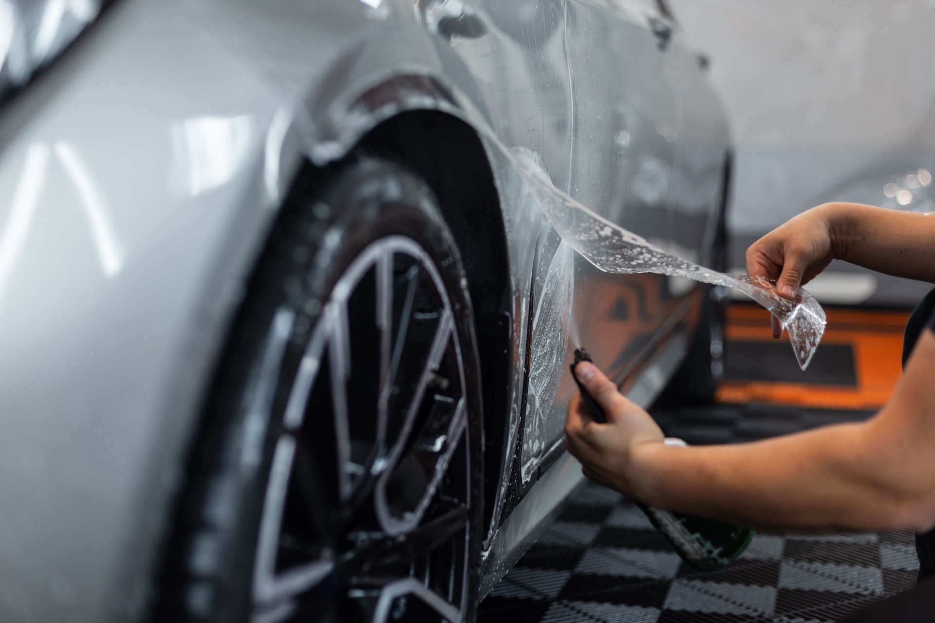 Professional man covers a car with protective film in a detailing center. Car protection and care